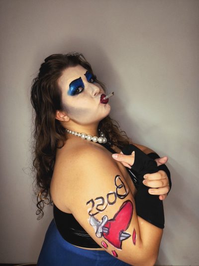 Maquillaje de Frank-N-Furter de perfil con cigarrillo y body paint "BOSS" en el brazo